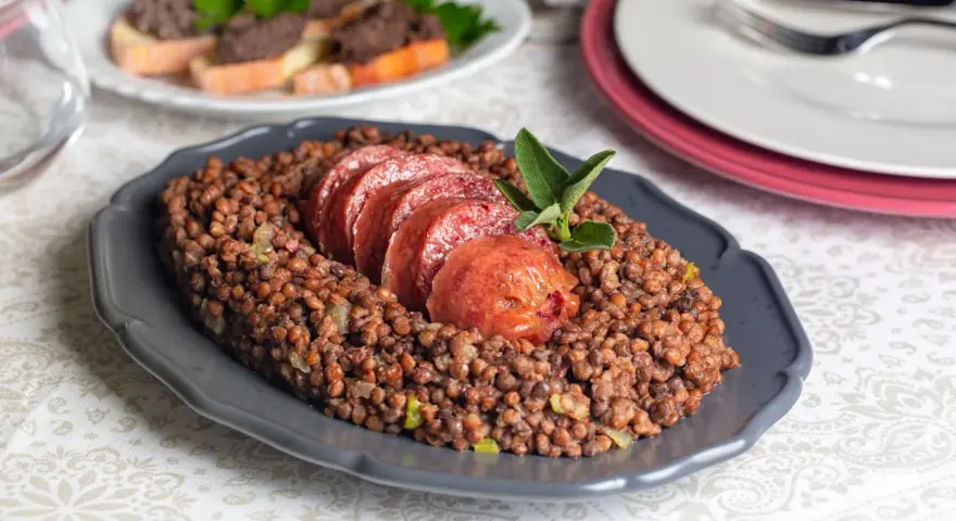 Piatto di lenticchie con fette di cotechino, un classico su come si fa il cotechino. Guarnito con salvia.