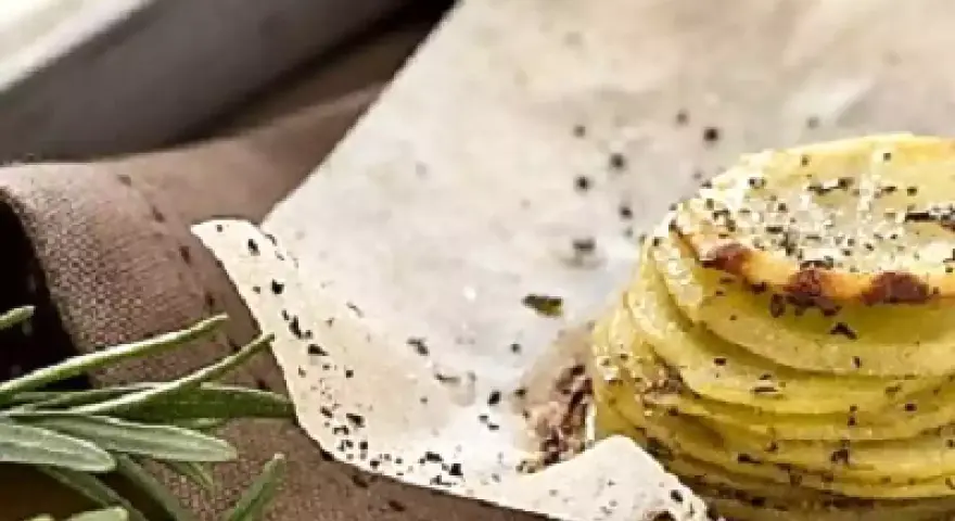 Deliziosa torretta di patate, sottili fette impilate e condite con erbe aromatiche e pepe nero, su carta da forno.