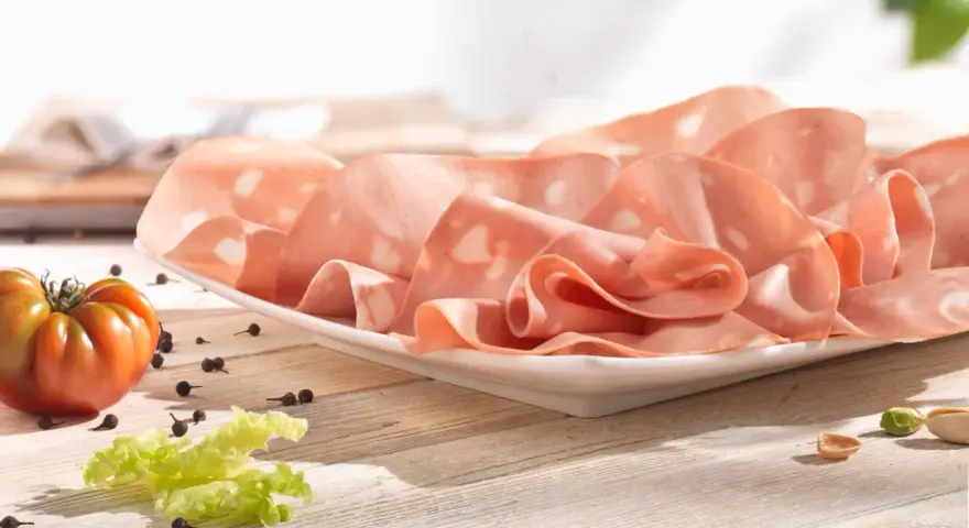 Fette di mortadella su piatto bianco, con pomodoro, lattuga e pepe. La differenza tra mortadella e bologna è nella qualità e negli ingredienti.