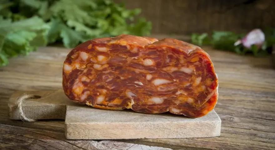 Un pezzo di salame stagionato su tagliere di legno. La differenza tra salame e sopressa è nella grana: qui si vede la carne tritata grossolanamente.