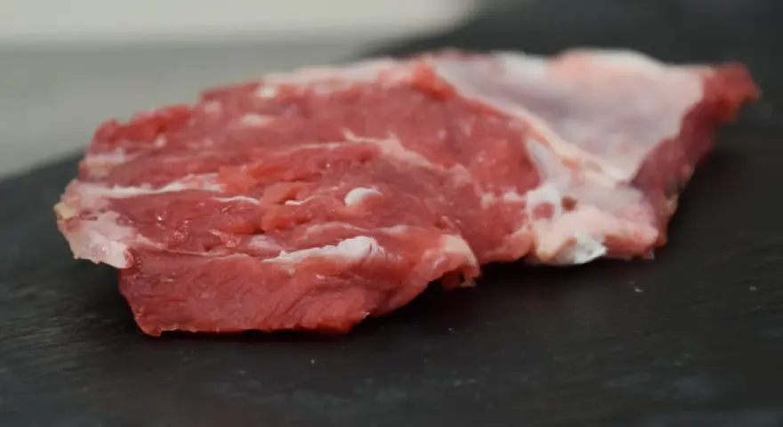 Un succulento spider steak crudo, con venature di grasso bianco, pronto per essere cucinato su una pietra scura.