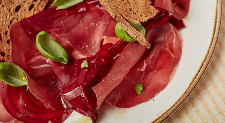 Fette di bresaola e barbabietola, esempi di salumi non insaccati quali sono, con crostini e basilico.