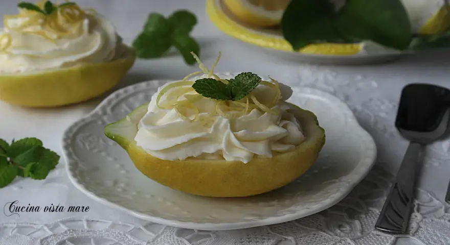 Deliziosa mousse al limone servita in un limone svuotato, guarnita con scorzette e menta.