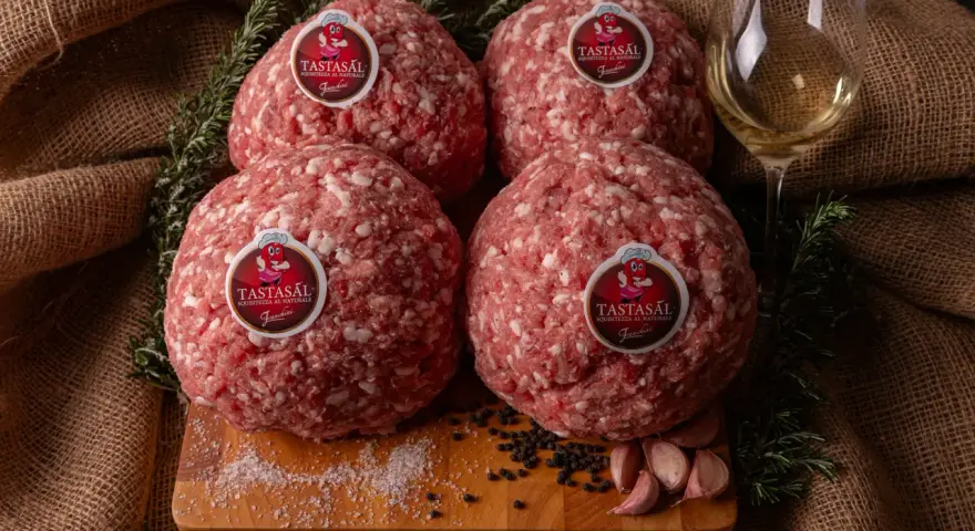 Quattro sfere di carne macinata TASTASAL, con rosmarino, aglio, pepe e sale su un tagliere. Ingredienti freschi per un sapore autentico.