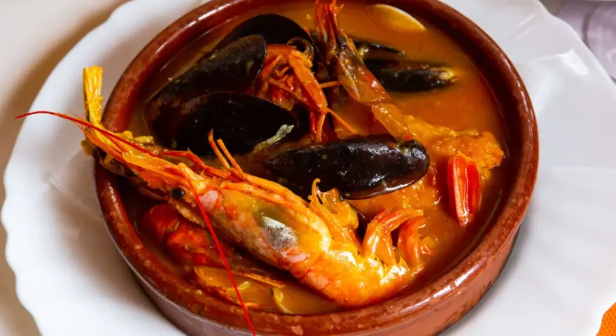 Una ricca zuppa di pesce in ciotola di terracotta, con gamberoni, cozze e pomodorini.