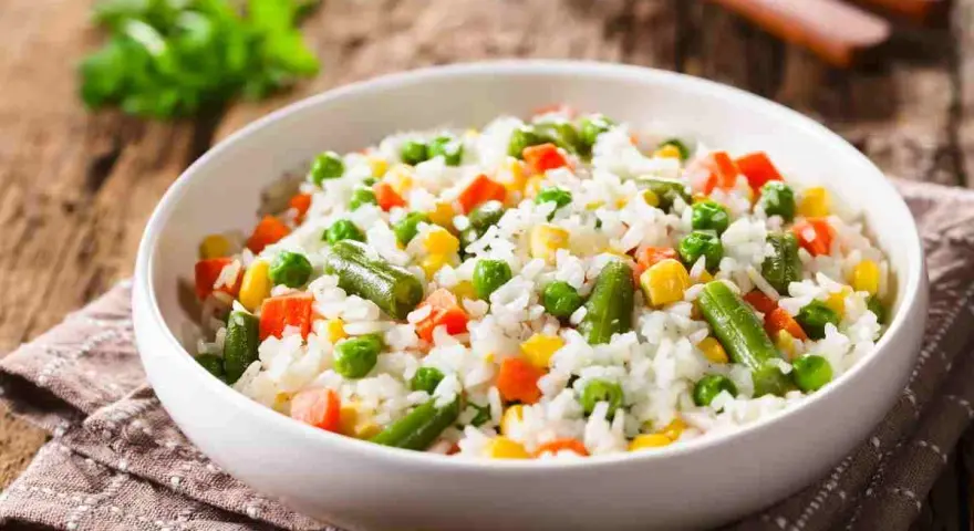 Un piatto di riso per insalata di riso, con piselli, carote, fagiolini e mais, su un tovagliolo di stoffa marrone.