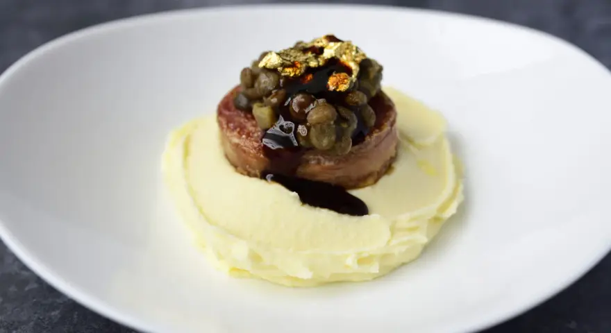 Piatto moderno con lenticchie e cotechino, un omaggio alla tradizione, servito su purè di patate e decorato con oro edule.
