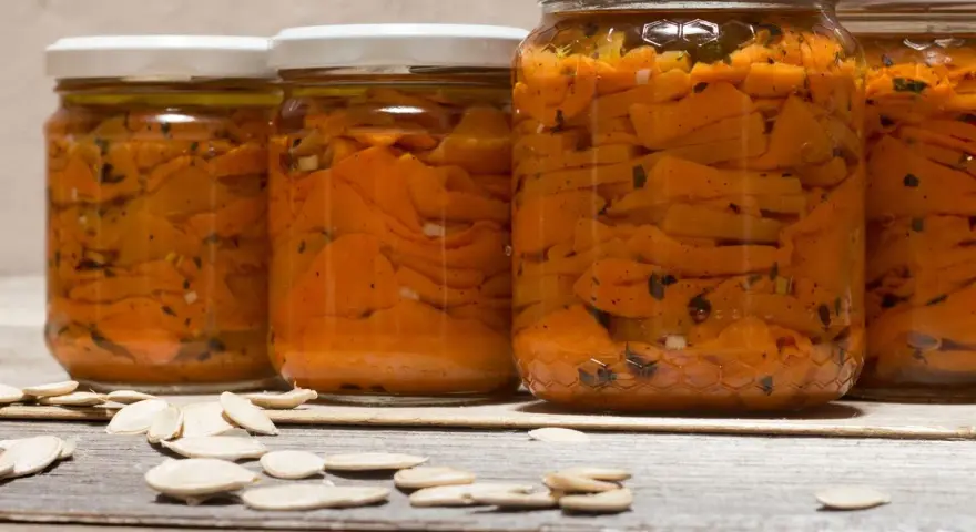 Barattoli di zucca sott'olio in agrodolce, con semi di zucca sparsi sul tavolo di legno.