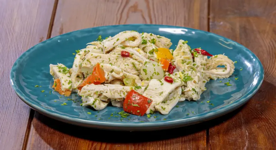 Piatto di insalata di trippa condita con erbe aromatiche, peperoncino e verdure colorate.