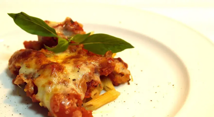 Porzione di pasta ncasciata fumante, con formaggio filante e basilico fresco, su un piatto bianco.