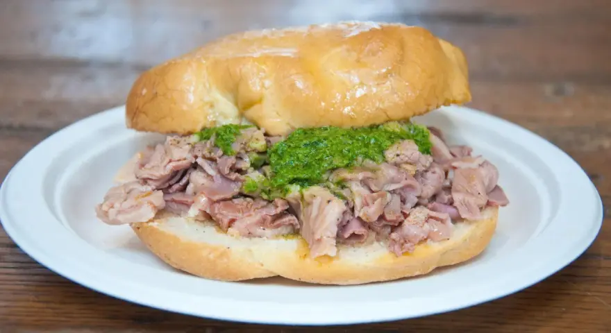 Panino con lampredotto, un classico street food fiorentino. La ricetta prevede trippa di bovino cotta e servita in un panino morbido con salsa verde.