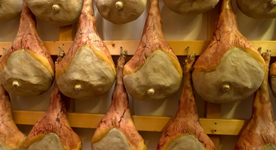 Filetti di salumi appesi a stagionare su scaffali di legno.