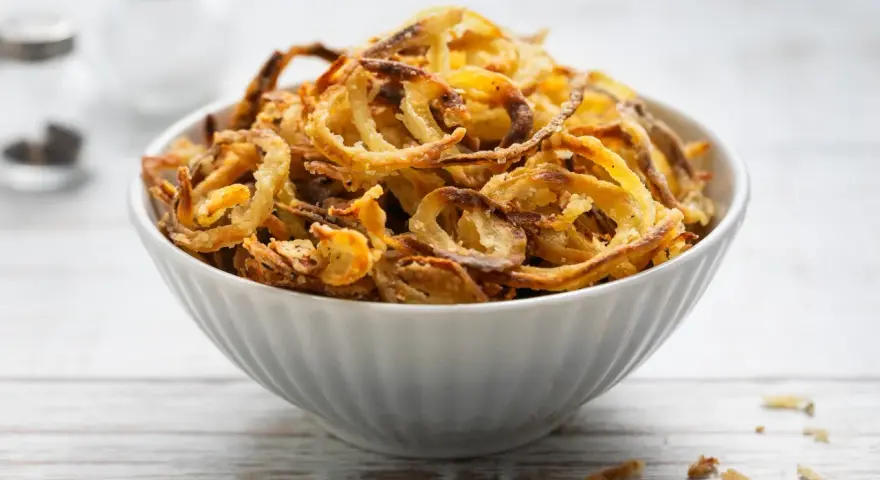 Ciotola piena di croccanti cipolle fritte dorate, perfette per accompagnare ogni piatto.