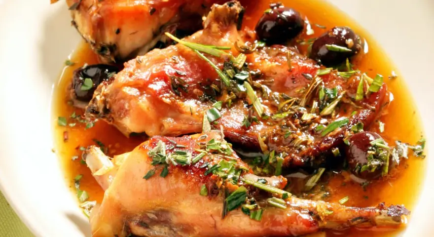Coniglio alla ligure succulento, con olive nere e erbe aromatiche, immerso in un sugo dorato.