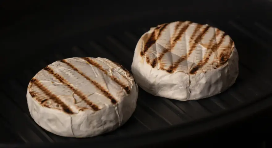 Due forme di formaggio da fare alla piastra, con belle striature dorate, cuociono in una padella scura.