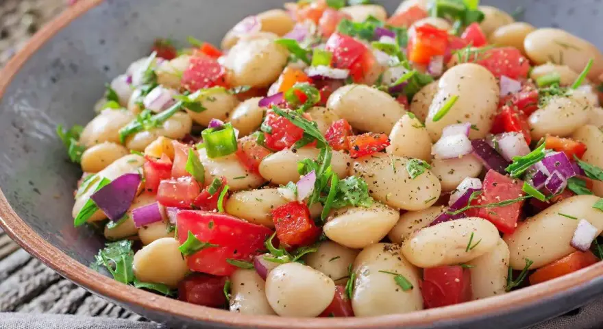 Insalata di fagioli bianchi, pomodori freschi, cipolla rossa e erbe aromatiche in una ciotola rustica. Un piatto colorato e salutare.