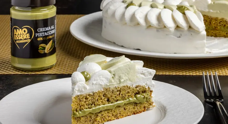 Una fetta di torta soffice al pistacchio, con crema al pistacchio e panna montata. Accanto, un barattolo di crema al pistacchio.