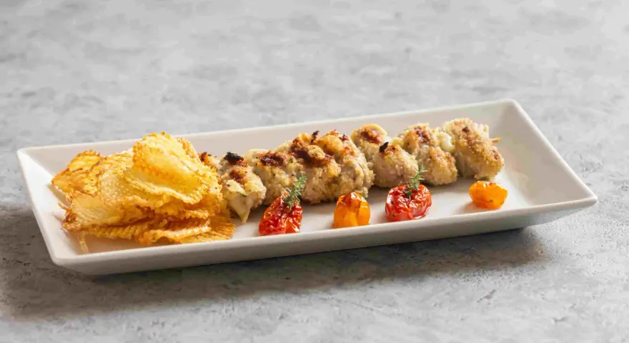 Involtini alla messinese su uno spiedino, accompagnati da patatine croccanti e pomodorini confit.