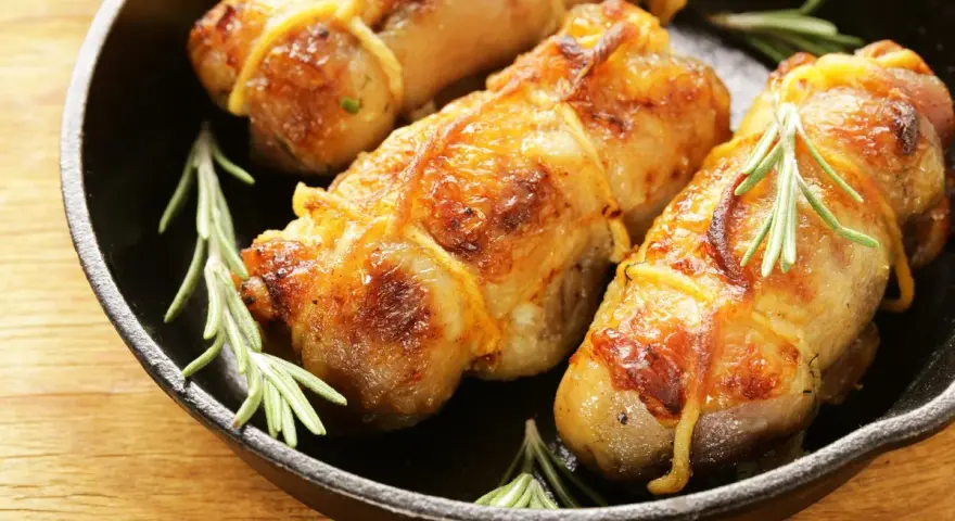 Involtini di pollo al forno dorati e succulenti, legati con spago da cucina e guarniti con rametti di rosmarino fresco, serviti in una padella di ghisa.