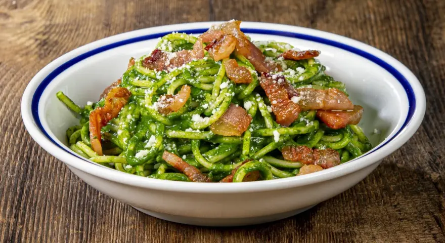 Un piatto invitante di pasta con spinaci, condita con croccante pancetta e parmigiano grattugiato, servita in una ciotola bianca con bordo blu.