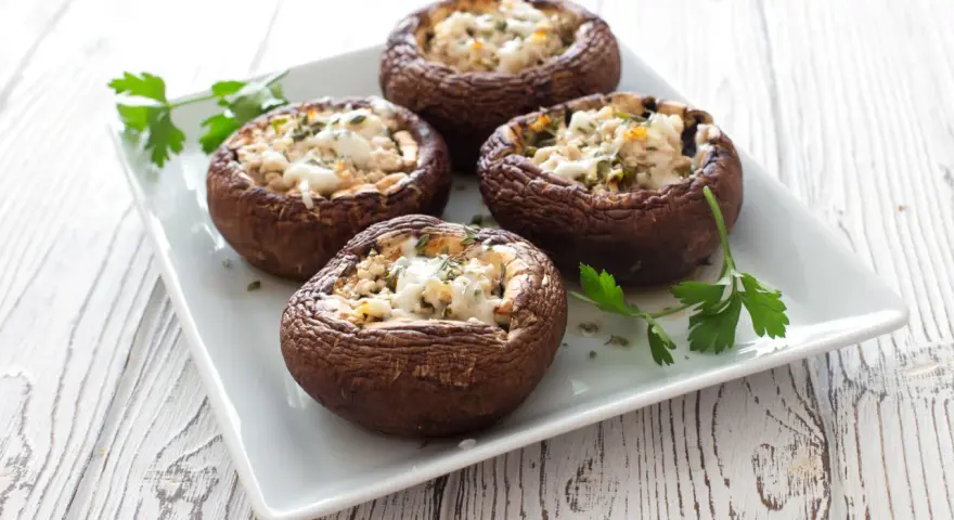 Quattro funghi ripieni al forno, dorati e invitanti, guarniti con prezzemolo fresco su un piatto bianco.