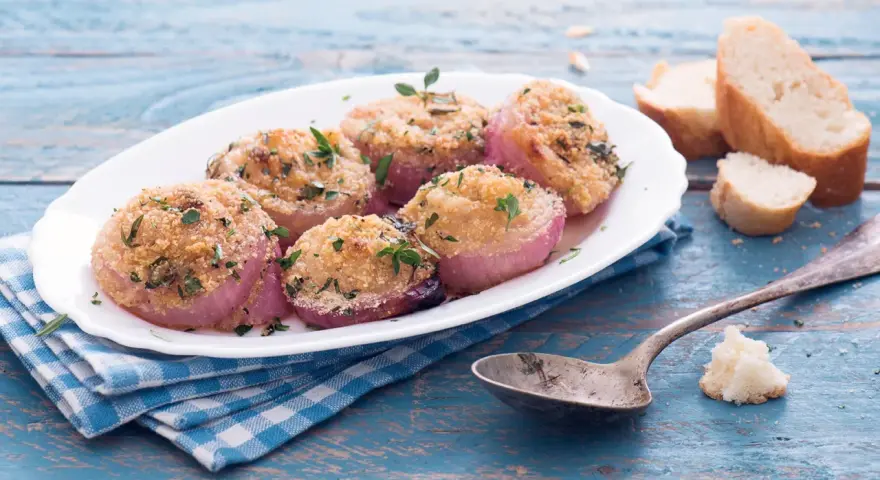 Deliziose cipolle al forno, dorate e profumate, servite su un piatto bianco con pane croccante e un cucchiaio d'argento.