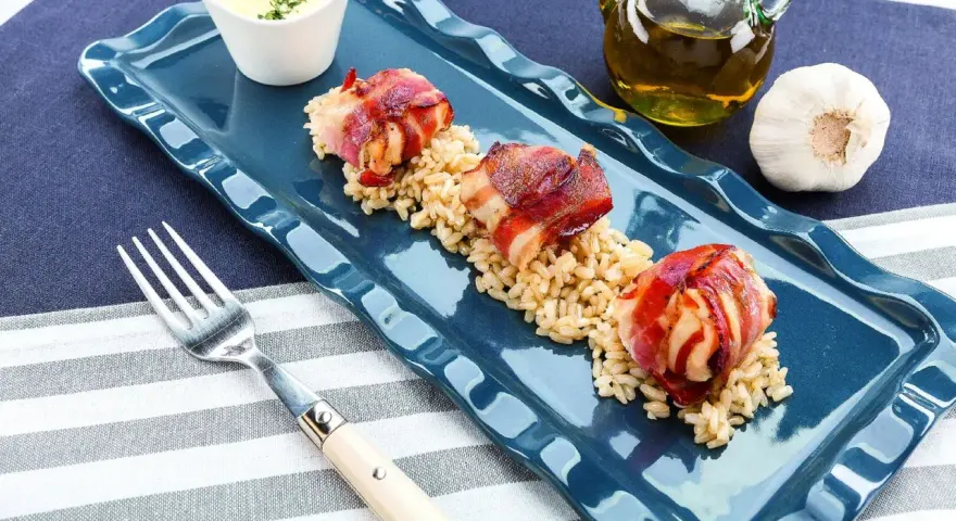 Tre bocconcini di pollo con pancetta avvolti e dorati, serviti su un letto di riso integrale.