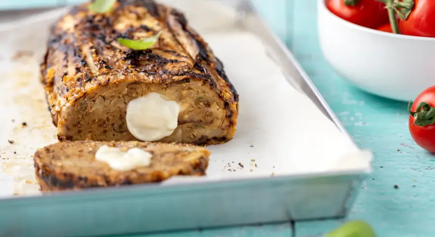 Polpettone di melanzane grigliato, ripieno di formaggio filante, su teglia con basilico e pomodorini.