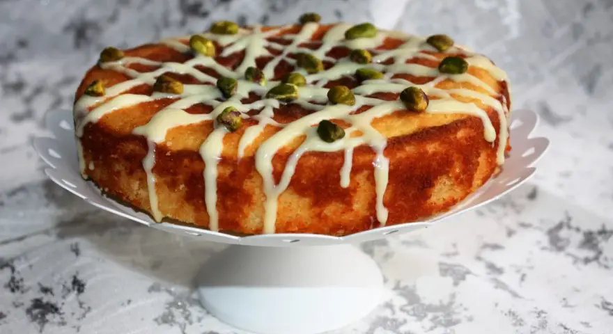 Deliziosa torta al bergamotto, decorata con glassa bianca e pistacchi croccanti, pronta per essere gustata.