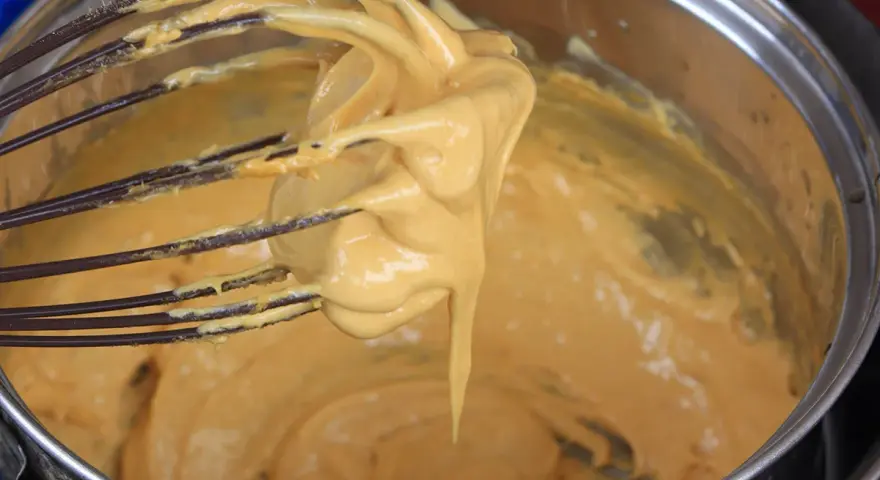 Una frusta raccoglie una crema densa e dorata, pronta per diventare uno zabaione freddo.