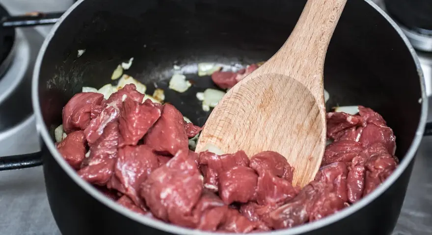 Bocconcini di manzo crudo in padella con cipolla, pronti per diventare uno spezzatino gommosa di manzo.
