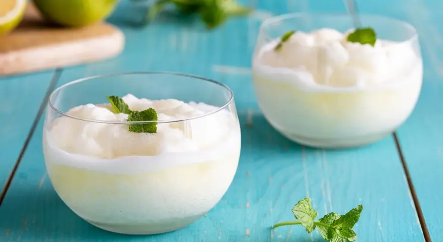 Sorbetto al limone senza gelatiera: due coppette di fresco sorbetto al limone guarnite con menta, su un tavolo di legno blu.