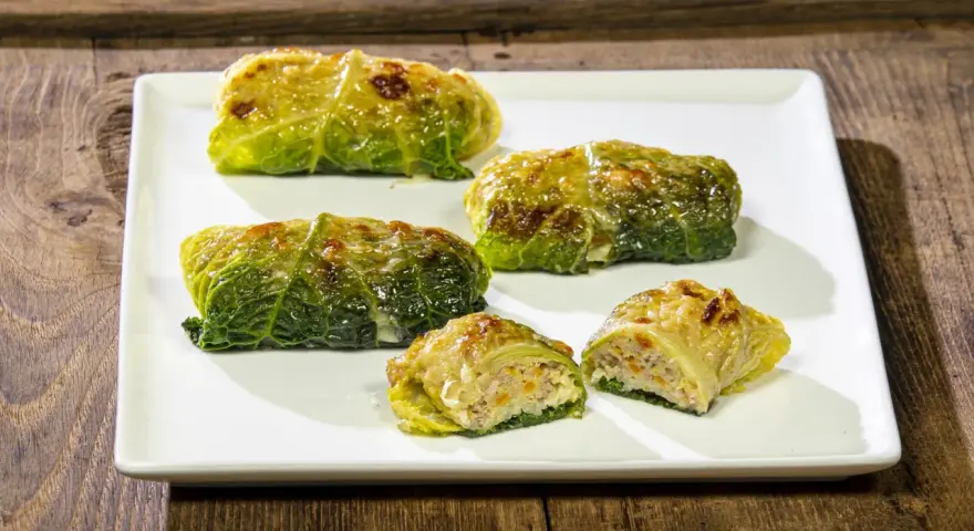 Cinque capunet piemontesi, involtini di verza ripieni, serviti su un piatto bianco.