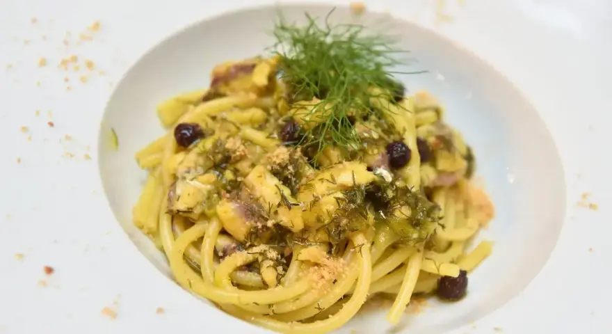 Un piatto invitante di pasta con finocchi, olive e acciughe, guarnito con erbe fresche e pangrattato.