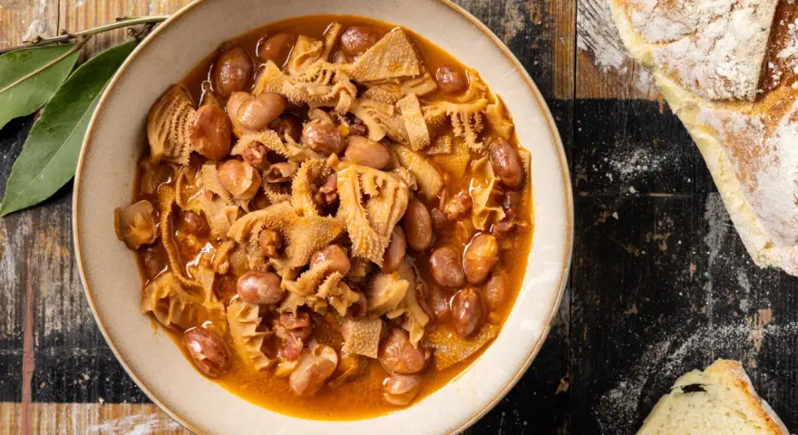 Piatto fumante di trippa alla milanese con fagioli, su un tavolo di legno rustico, accanto a pane casereccio.