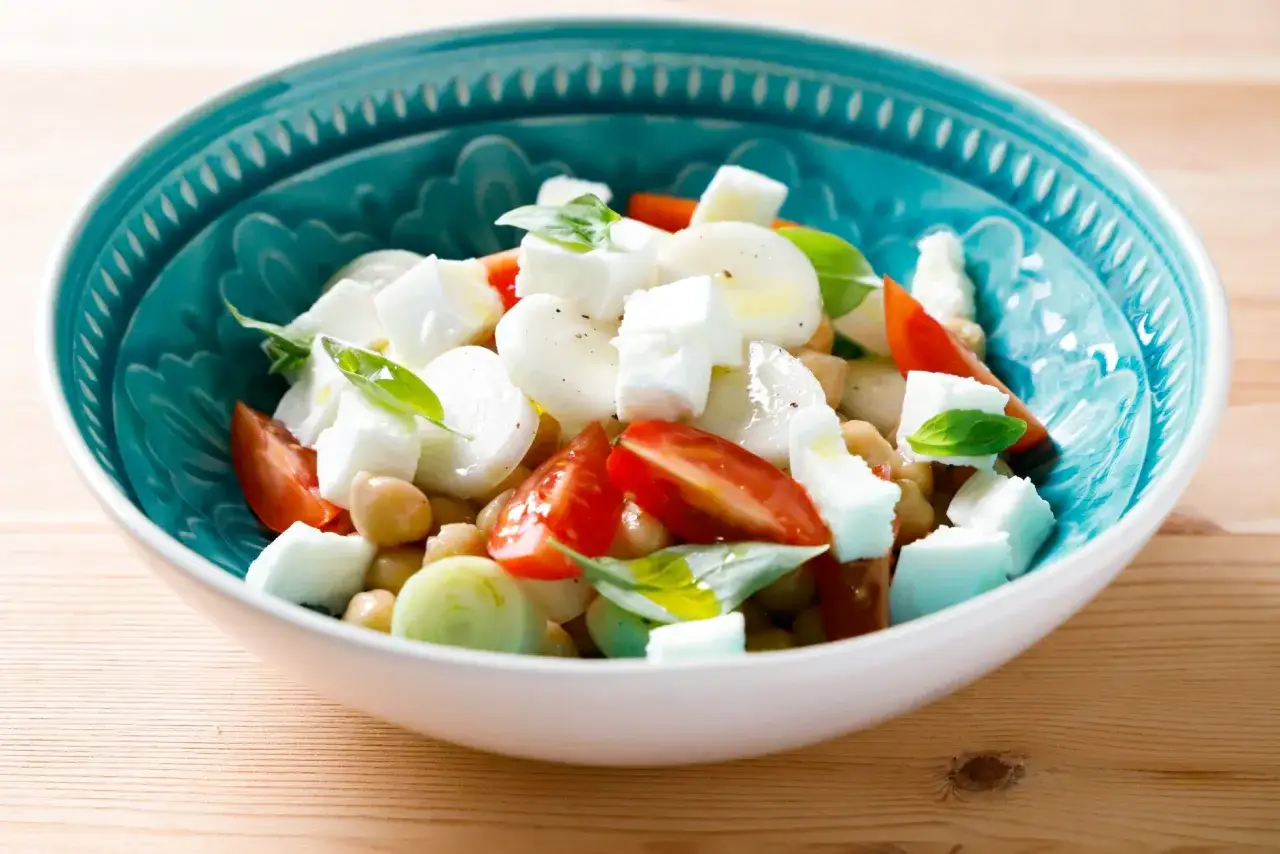 Insalata di ceci con pomodorini, mozzarella e basilico in una ciotola blu decorata. Fresca e colorata, perfetta per un pasto leggero.