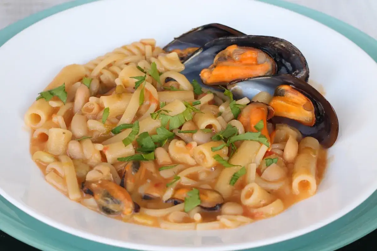 Un piatto invitante di pasta fagioli e cozze, con pasta corta, fagioli bianchi e cozze nere in un sugo saporito, guarnito con prezzemolo fresco.