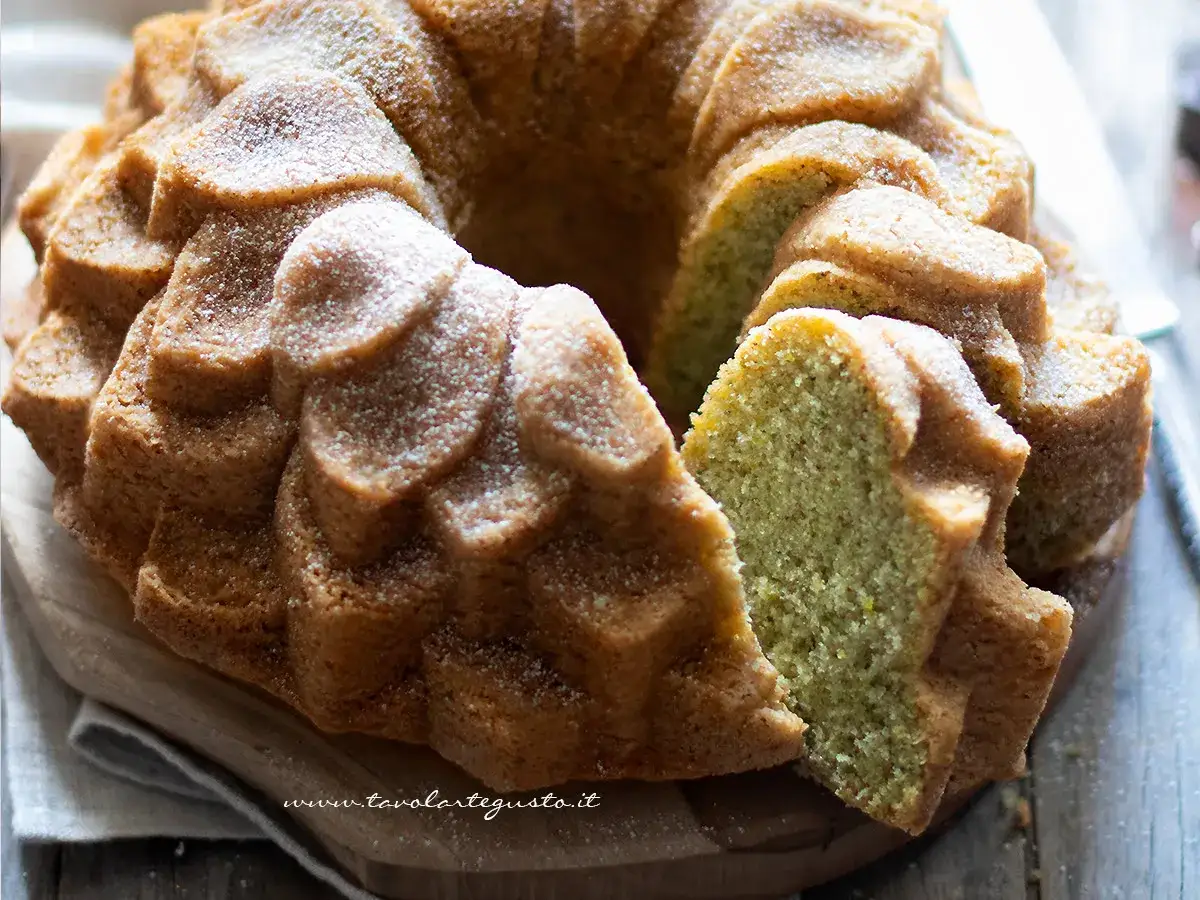 Una fetta di torta soffice al pistacchio, cosparsa di zucchero a velo, mostra la sua mollica verde e invitante.