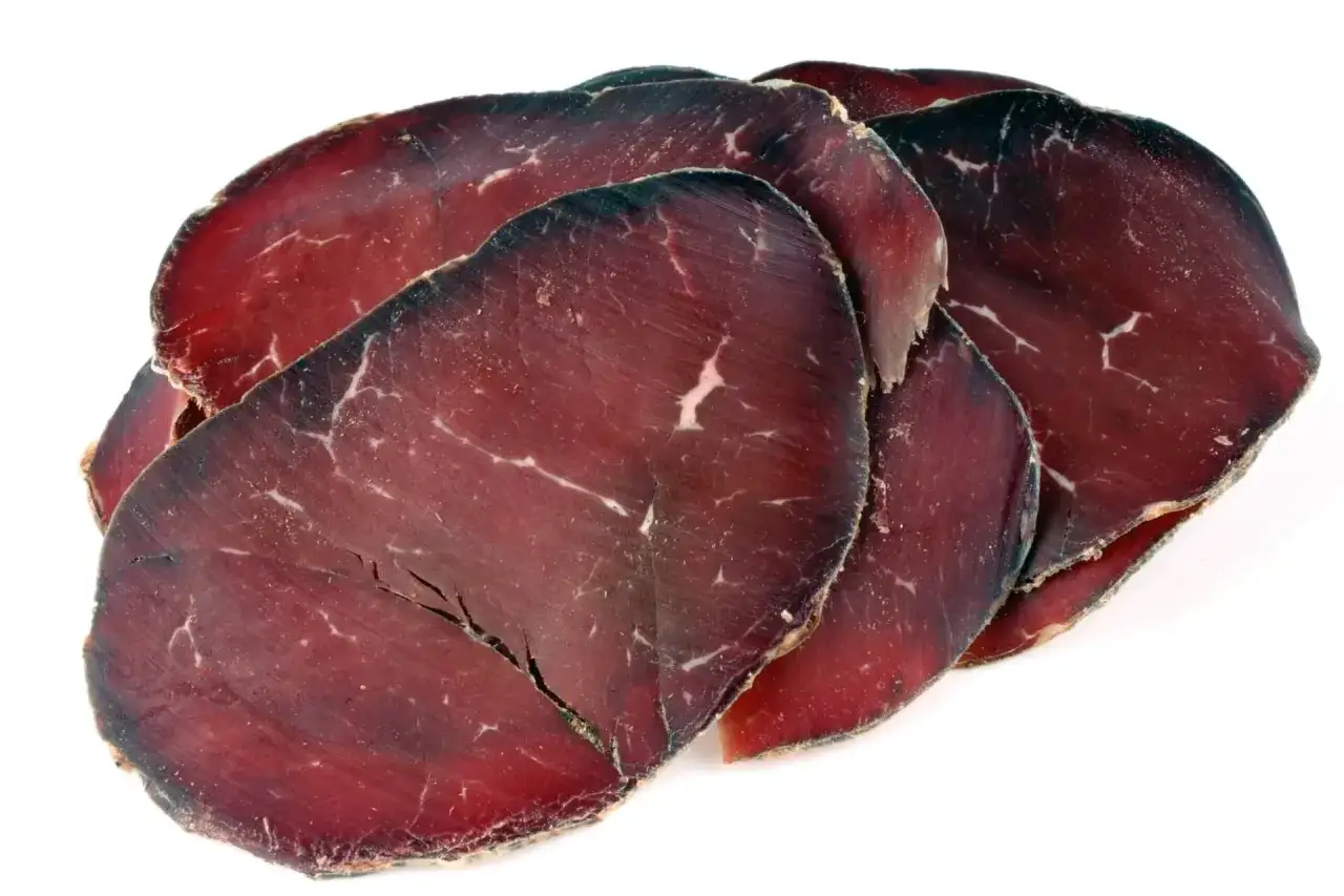 Fette di bresaola scura, forse di cavallo, su sfondo bianco. Meglio bresaola di cavallo o manzo? Un dilemma per gli amanti dei salumi.