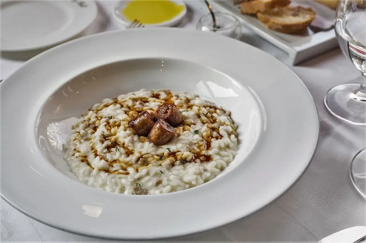Un cremoso risotto alla monzese, guarnito con salsiccia e erbe aromatiche, servito in un piatto bianco.