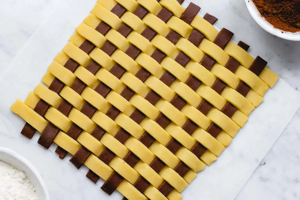 Ecco come mettere le strisce sulla crostata: un intreccio di pasta chiara e scura crea un motivo a griglia perfetto per decorare.