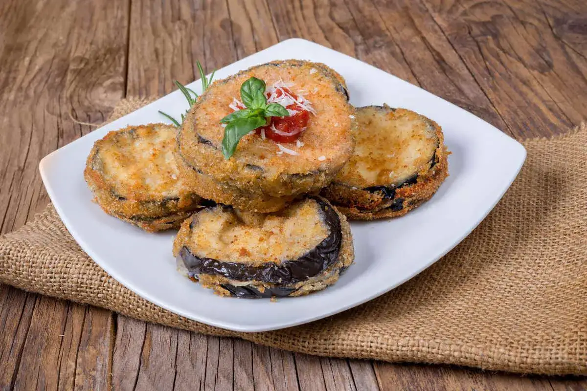 Fette di melanzane impanate e fritte, guarnite con pomodoro e basilico, pronte per essere gustate come melanzane alla pullastiello.