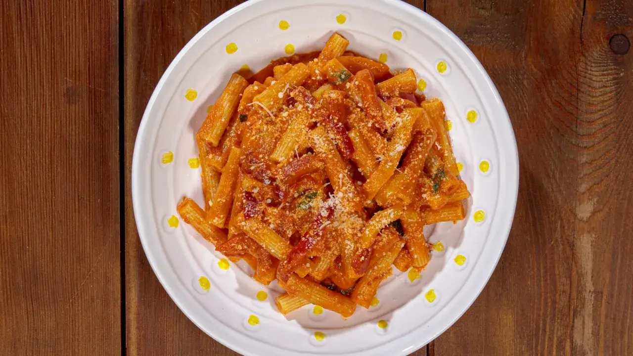 Piatto di pasta con i peperoni alla pugliese, condita con sugo rosso e formaggio grattugiato, servita su un piatto bianco con decorazioni gialle.
