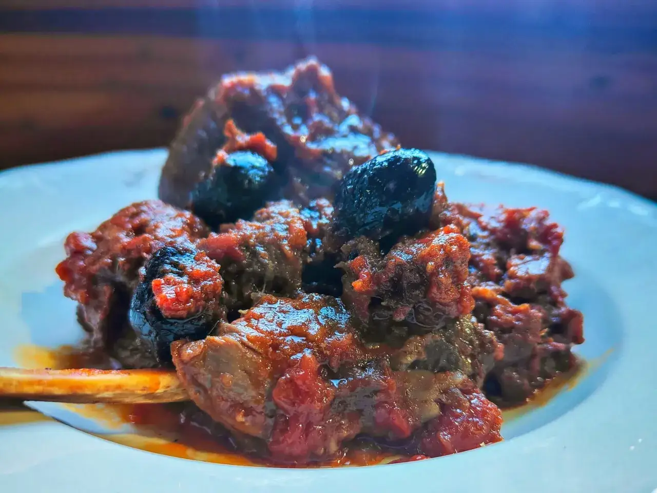 Piatto fumante di cinghiale in umido fatto in casa da Benedetta, con olive nere e un osso in evidenza.