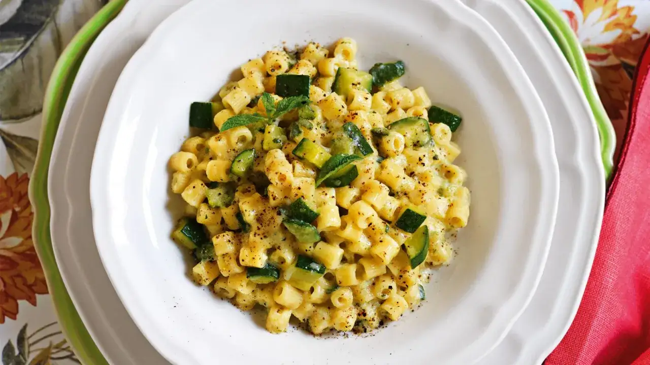 Un piatto di pasta cremosa con zucchine a cubetti, un'ottima carbonara di zucchine, guarnita con menta fresca e pepe nero.