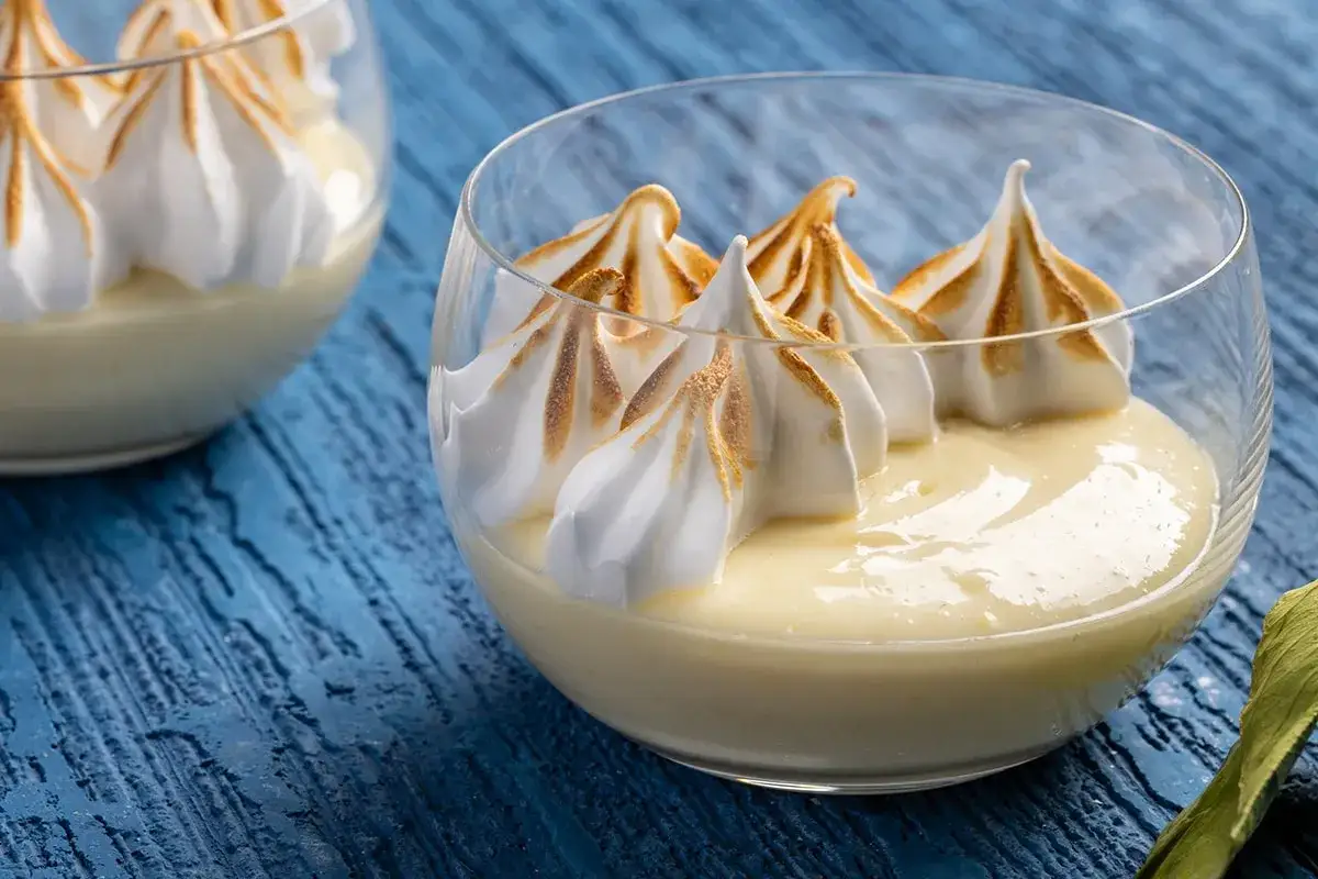 Coppette di mousse al limone con meringa dorata, servite su un tavolo blu.