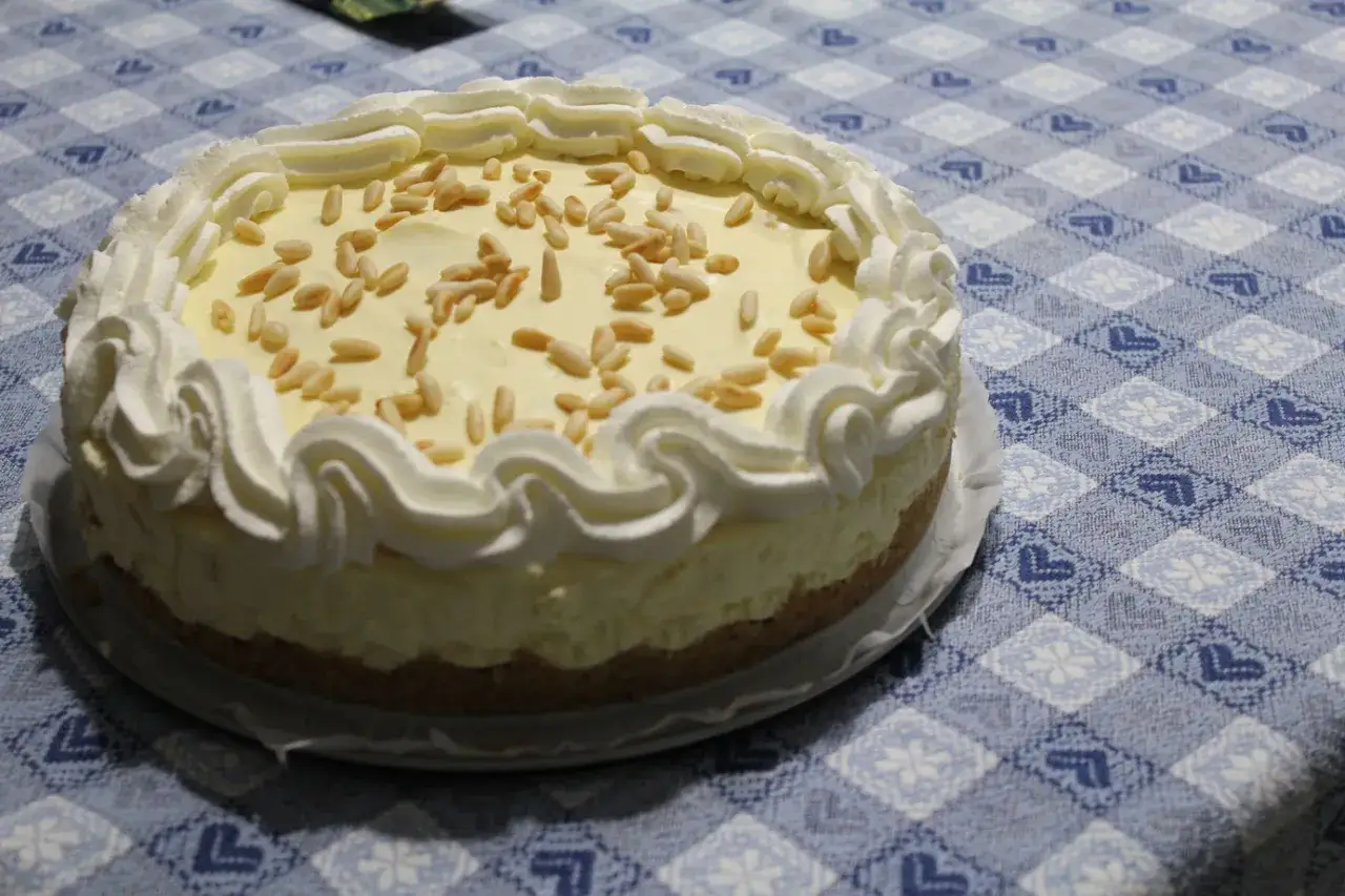Deliziosa torta biscotto con crema gialla e pinoli, decorata con panna montata.