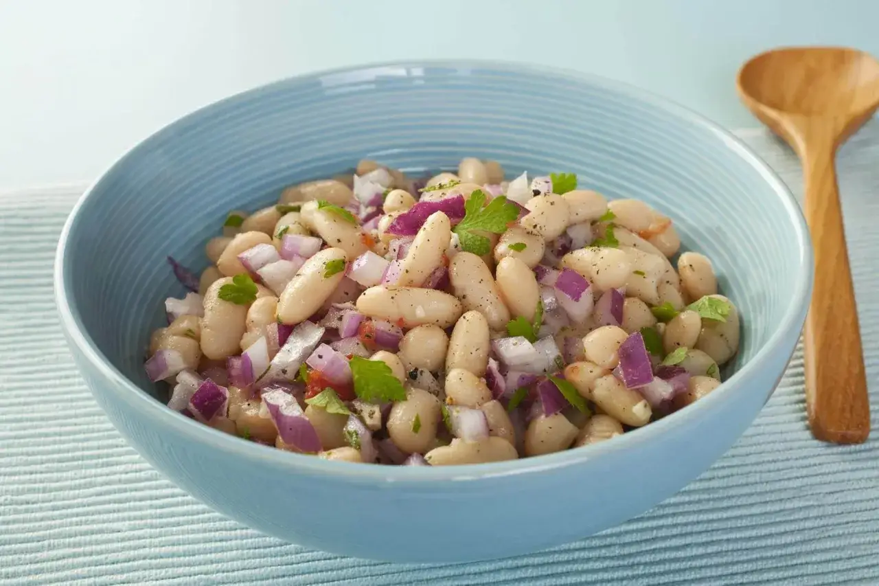 Insalata di fagioli bianchi con cipolla rossa tritata e prezzemolo, servita in una ciotola azzurra.
