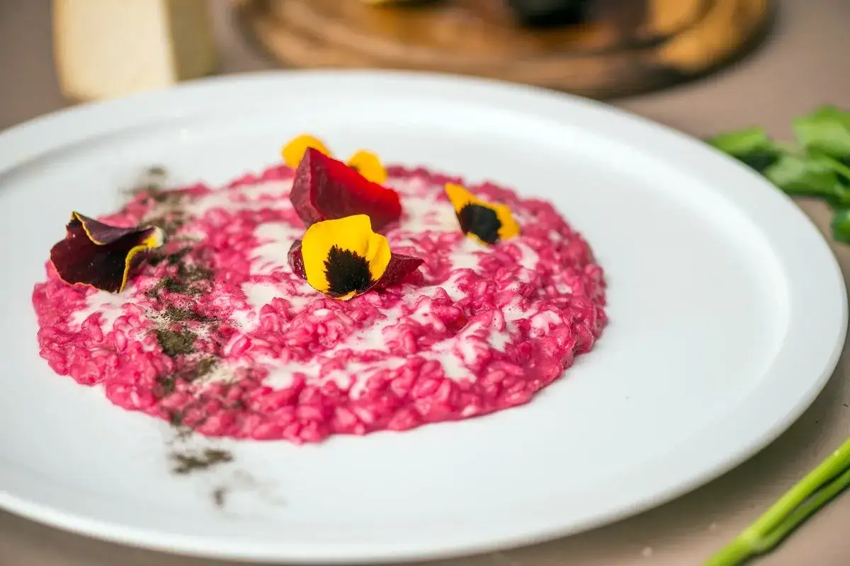 Risotto barbabietola e gorgonzola, un piatto vibrante con fiori eduli e cubetti di barbabietola.