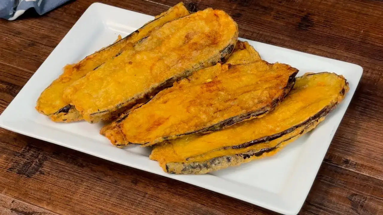 Fette di melanzane fritte, dorate e croccanti, servite su un piatto bianco. Un assaggio delle melanzane alla pullastiello.